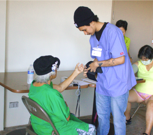 Isaiah Stagner, a high school occupational therapy student, helps a kūpuna measure their blood pressure.